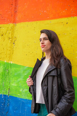 Photograph of a transsexual woman in front of a wall with the rainbow gay flag. We activate LGTBIQ+