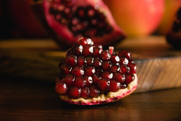 Juicy piece of pomegranate macro and apple on cutting board on dark background.