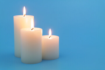 Fototapeta na wymiar White scented candles burning on blue background. 