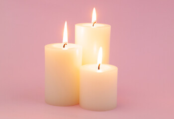 Obraz na płótnie Canvas Three white candles with different size burning on pink.