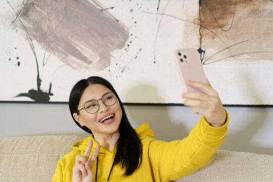 Asian student takes selfie with smartphone, utilizing the latest in mobile photography and communication technology. With glasses on, she captures self-portrait to share on social media or with