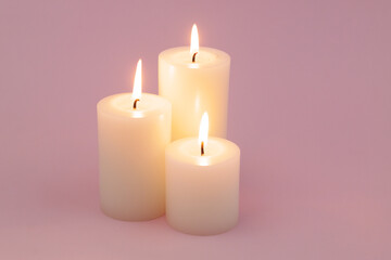 Obraz na płótnie Canvas White candles with different size melting and burning on pink background. 