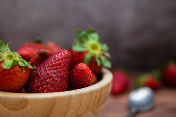 Sweet red strawberries in a wooden bowl placed on a table. Teaspoon and selective focus.