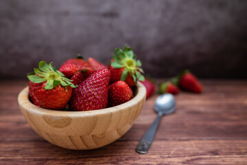 Sweet red strawberries in a wooden bowl placed on a table. Teaspoon and selective focus.