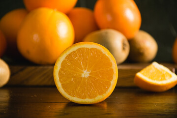 Fruits on a dark background. Half orange macro, oranges and kiwi on cutting board