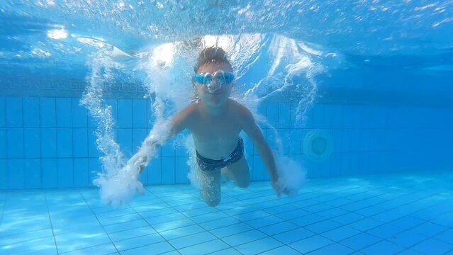 A happy boy dives into the pool, swims underwater in a beautiful pool with safety glasses on a sunny summer day