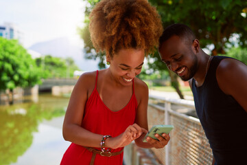 young afro black brazilian heterosexual couple using a cell phone and having fun outdoors in a park in Ipanema, Rio de Janeiro	