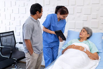 Nurse showing medical insurance data in digital tablet near bed of patient with relative stand by