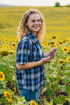 Portrait Of Woman Farmer Standing In A Sunflower Field With A Tablet And A Cell Phone Looking At The Camera And Smiling. Communication Concept. Business