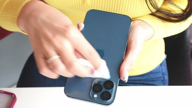 Smila, Cherkasy oblast,Ukraine -04.02.23:Hands of girl wiping Iphone 13 with disposable wet wipe, smartphone disinfection