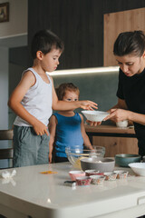 Cute little children helping mother to make dough for cookies, cooking together in cozy kitchen. Happy family day.