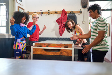 Happy young friends playing foosball in game room