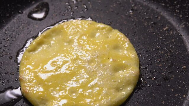 A round egg yolk pancake is flipped over in a hot frying pan