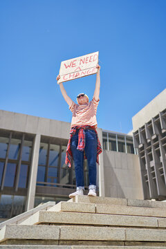 Young male protester holding change sign below government building