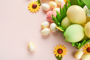 Happy Easter. Easter eggs and rabbit in green basket on pink background with white and yellow roses. Spring Happy Easter holiday card.  Easter background with copy space. Top view.