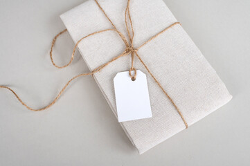Tag mockup on folded cotton fabric, new beige clothes with blank clothes tag on white background