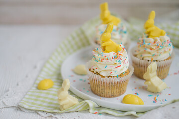 Lemon poppy seeds cupcakes with white whipped buttercream and white and yellow chocolate bunnies and coloreful sprinkles easter baking close up selective focus