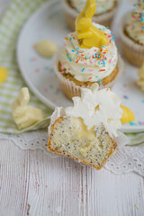 Lemon poppy seeds cupcakes with white whipped buttercream and white and yellow chocolate bunnies and coloreful sprinkles easter baking close up selective focus
