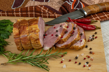 On a wooden cutting board, sliced juicy pork ham, carving knife, red hot peppers, multi-colored allspice, parsley, dill and basil. The concept of delicious pork products
