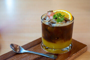 A glass of iced americano black coffee and layer of orange with sliced orange fruit