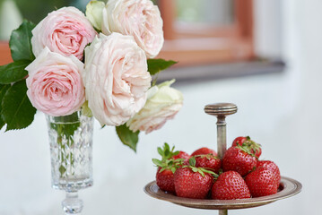 Fresh and organic strawberries in a silverware on the marble table with roses surround by greens....