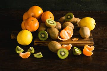 Sweet fruits on a dark background. Tangerines, lemons, kiwis, whole fruits and pieces on a wooden cutting board