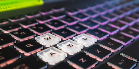 Highlighted gaming keys with pink purple gradient light and blurred background. Powerful dark notebook keyboard close-up. Tech, IT,  e-sport, computer science background