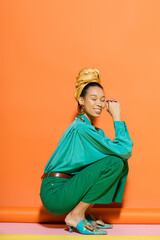 Carefree african american woman in bright clothes sitting near colorful background.