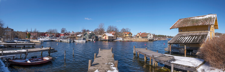 Obraz premium Cliffs and jetty houses at the bay Norrhamnen in the island Vaxholm, melting snow, a sunny spring day in Stockholm