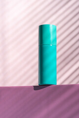 A blue bottle stands on a pink box against a pink wall