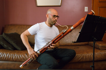 young latin man sitting playing the bassoon, reading and studying sheet music at home