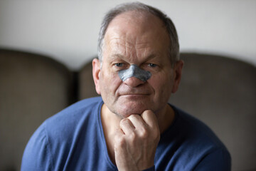 Smiling senior man applying black nose patch to clean pore skin and remove acne or blackheads on...