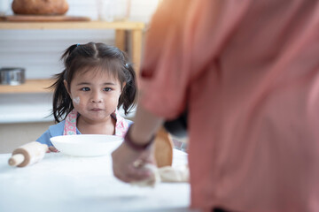 Little cute girl looking her mom make bakery in kitchen