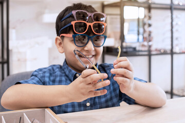 Funny Indian boy show eyeglasses on his face in optical store, Asian child boy selecting and trying on glasses in optical shop