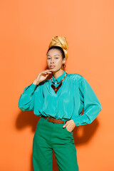Fashionable african american model in bright outfit standing on orange background.