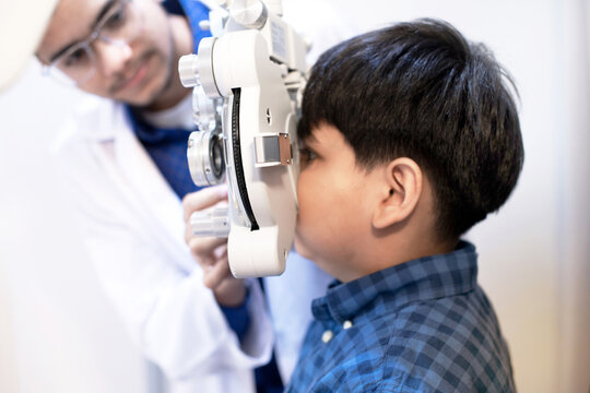 Indian boy doing eye test checking examination with optometrist in optical shop, side view, diagnostic ophthalmology equipment