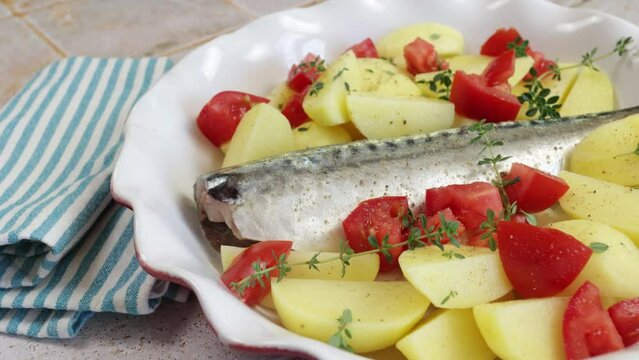 poisson (maquereau) avec pommes de terre, tomate, thym et oignons dans un plat