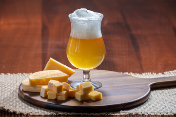 Glass of Belgian light blonde beer made in abbey and wooden board with variety of belgian cheeses