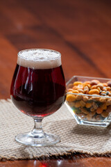 Glass of Belgian abbey red brown beer and glass bowl with party nuts