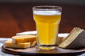 Glass of Belgian white unfiltered beer with notes of coriander and orange peer and wooden board with variety of belgian cheeses