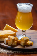 Glass of Belgian light blonde beer made in abbey and wooden board with variety of belgian cheeses