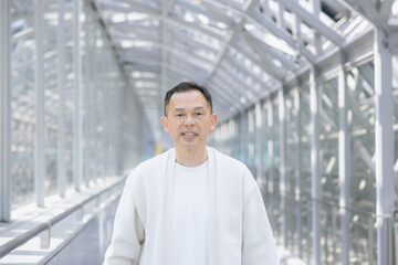 A middle-aged Asian man walks down a glass-walled hallway.