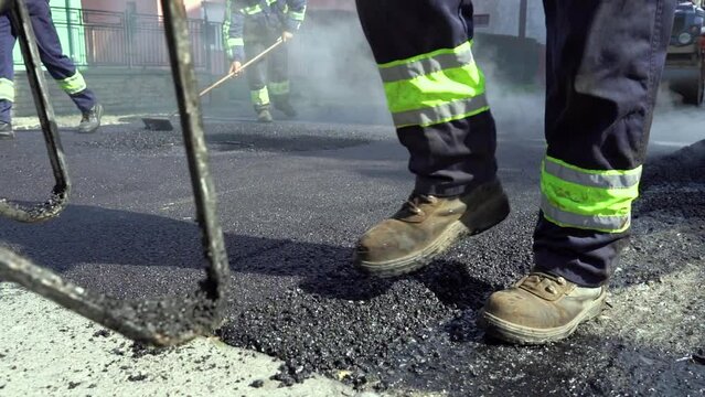 Road Worker Pushing a Wheelbarrow Over Hot Tarmac in Slow Motion. Men Working On Tarmac Road Maintenance. Steam is Rising from the Hot Asphalt Surface. Worker Leveling Fresh Asphalt. Road Construction