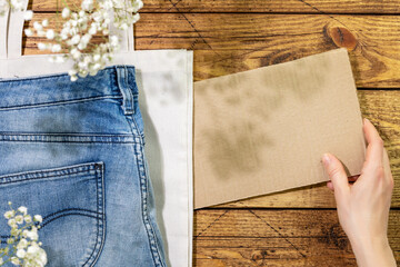 Sustainable still life with jeans on textile bag and female hand holding empty cardboard for your text. Second hand shop. Circular fashion, eco friendly shopping, thrifty shop concept. Copy space