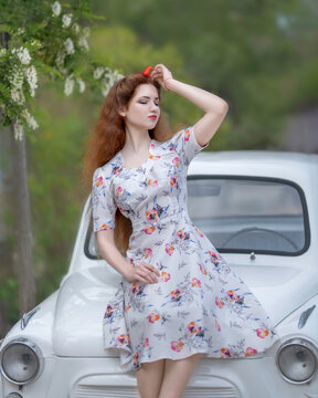 Portrait of a girl in a summer dress on the hood of a retro car