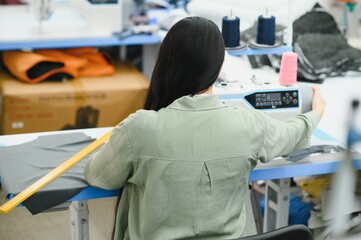 Positive young woman sewing with professional machine at workshop.