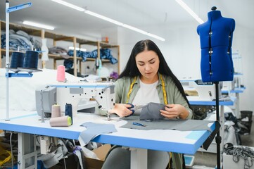 Naklejka premium Happy attractive young woman seamstress sitting and sews on sewing machine in studio