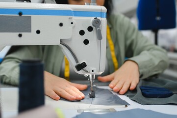 Happy female dressmaker working with sewing machine at textile factory.