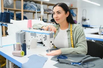 Obraz premium Happy female dressmaker working with sewing machine at textile factory.