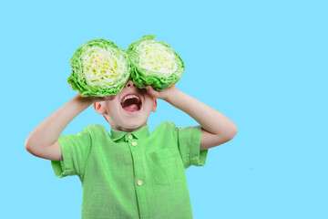 a Happy cute boy is having fun played with green cabbage on yellow background wall.